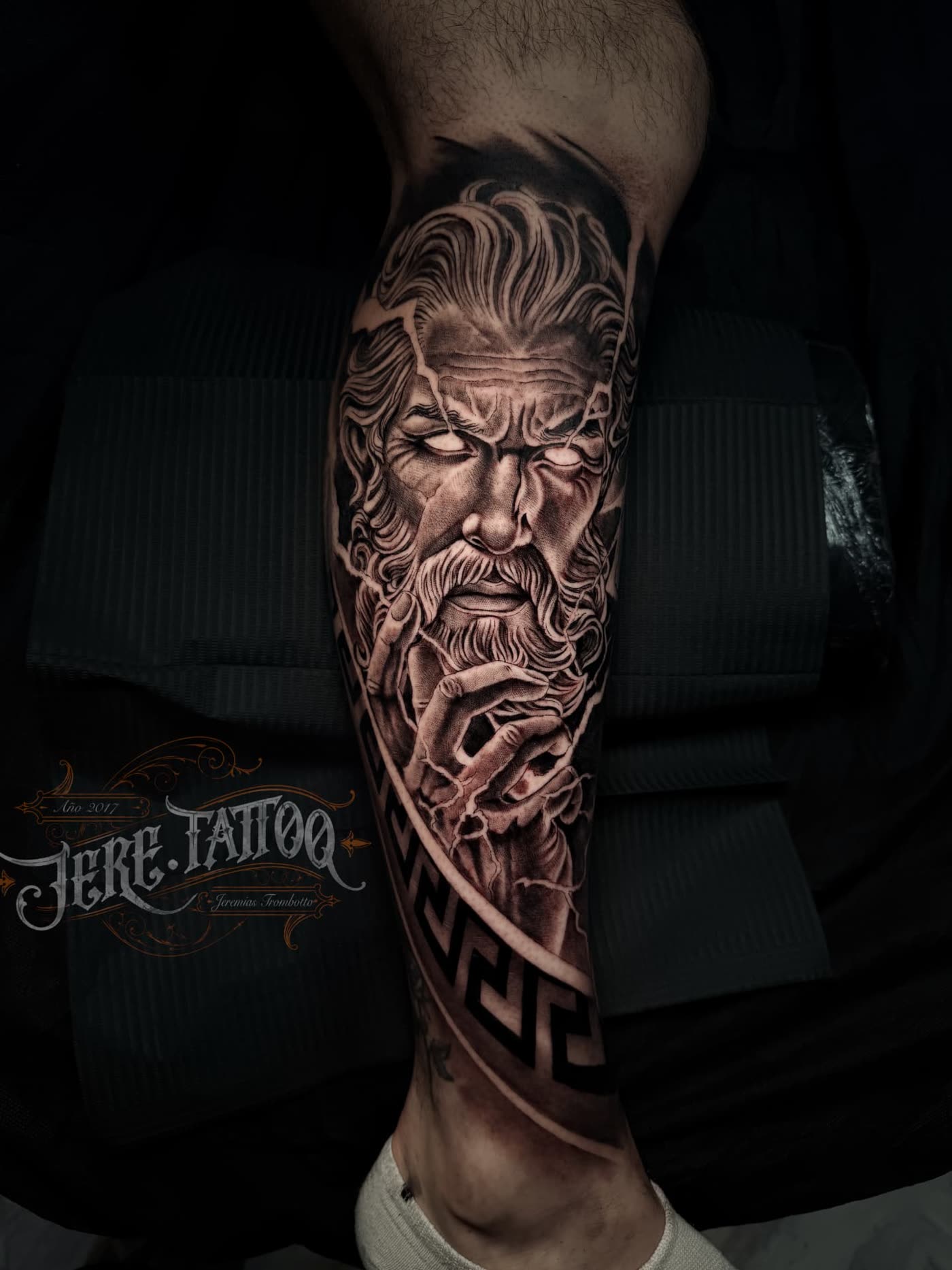 Tatuaje realista de Zeus con rayos y greca griega en la pierna, black and grey en Castellón